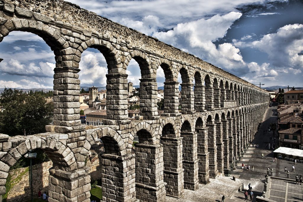 foto del acueducto romano de Segovia en la que se ven dos niveles de arcos semicirculares sobre pilares bien altos; la estructura es toda de piedra, y extiende por millas de un lado del valle al centro de la ciudad.