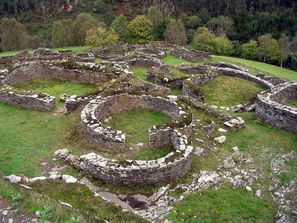 Ruinas de las casas del Castro en Coaña, Asturias, mostrando las paredes circulares de piedra; también se nota que el castro fue ubicado encima de una colina.