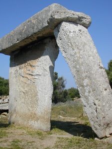 foto de taula, que consiste en un pilar ancho vertical y otro más angosto inclinado, ambos reuniéndose bajo una enorme piedra rectangular horizontal