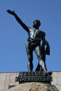 foto de una escultura en bronce de Viriato; lleva solamente un taparrabo (loincloth), al estilo de los guerreros celtas, levanta la mano derecha en un saludo y tiene su espada agarrada en la mano izquierda.