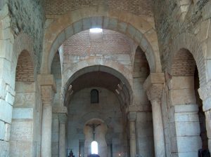 Interior de la iglesia mostrando varios arcos de herradura que sostienen el techo de la nave, todo hecho de piedra. Los arcos tienen la forma de herradura típica de los visigodos.