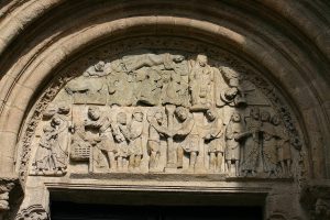 Detalle de relieve escultural sobre una puerta en la Catedral de Santiago de Compostela, mostrando muchas figuras humanas y una borde de elementos florales.