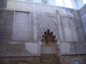 foto de un muro interior con decoraciones geométricas en yeso y una puerta cuya parte superior tiene sub-arcos circulares
