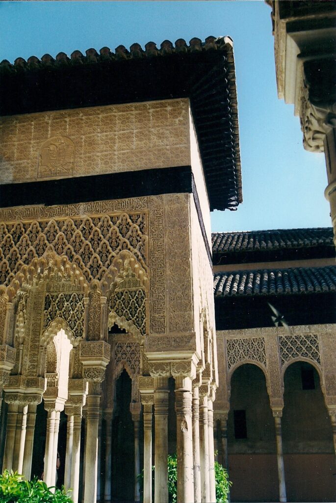 Foto mirando hacia arriba a las columnas delicadas que apoyan el techo de la entrada a la Sala de los Abencerrajes; los arcos y muros entre las columnas llevan decoraciones intrincadas geométricas e inscripciones en letras árabes.