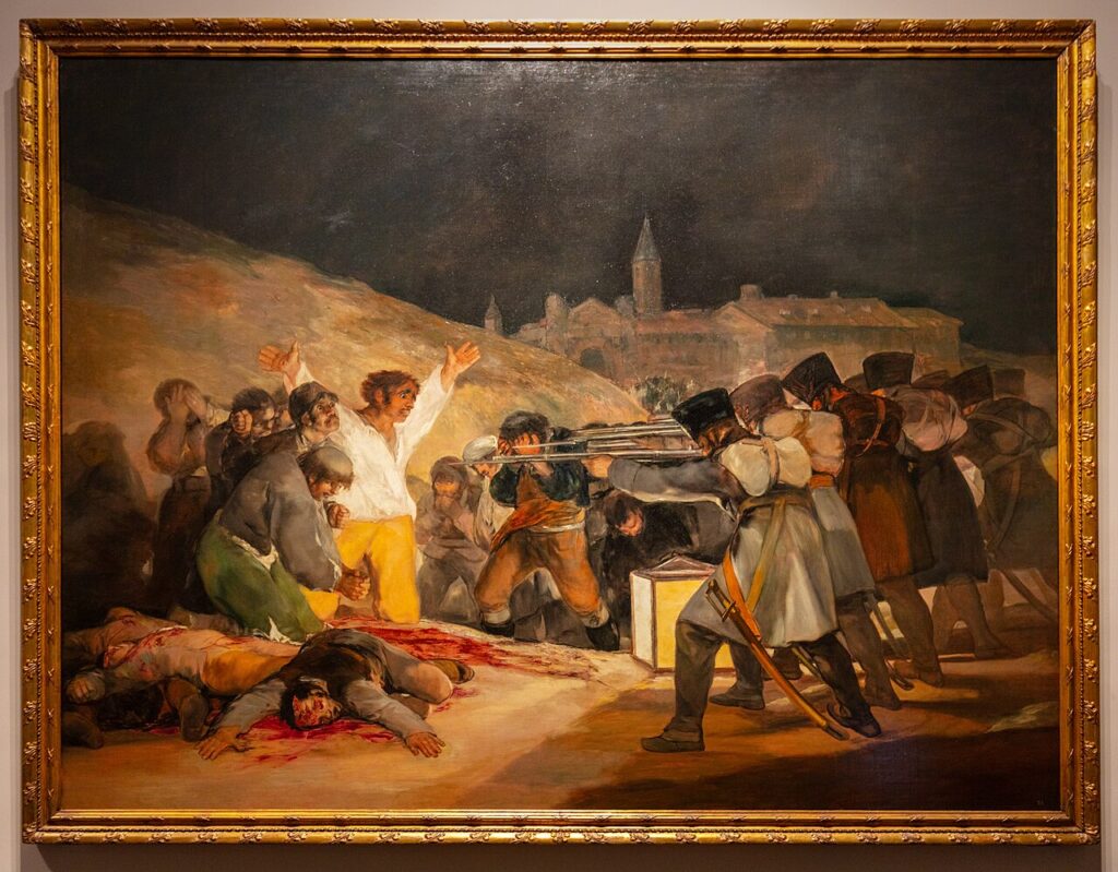 en la pintura una línea de soldados franceses apuntan sus fusiles a un grupo de personas, todos llenos de terror, especialmente un hombre en camisa blanca que levanta sus manos y un fraile que se arrodilla rezando