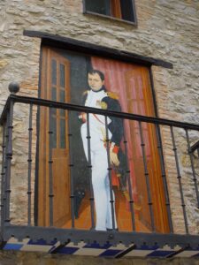 foto de un panel pintado en la pared de una casa de piedra con una reproducción de un retrato famoso de Napoleón, como si estuviera parado de pie en el balcón